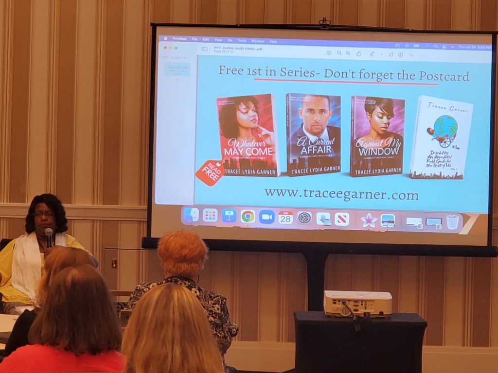 Tracee speaks in front of the room next to her slide presentation featuring four of her books.