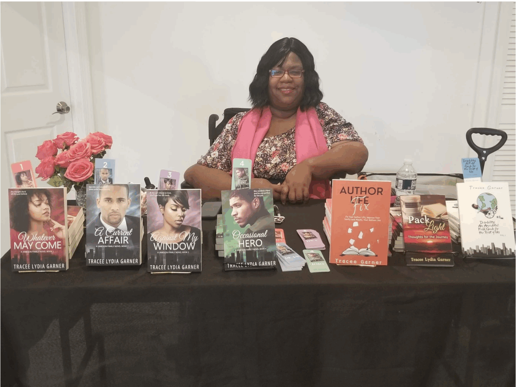 Tracee sits behind a table with her books, flowers lined up on top.